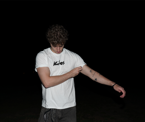 Man wearing a white KILOS t-shirt with a brand logo on a black background