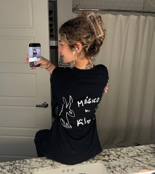 Girl taking a mirror selfie in a bathroom wearing a black KILOS shirt 