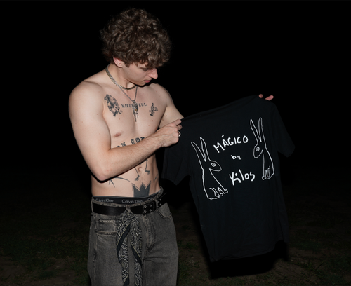 Man holding a black KILOS clothing t-shirt against a dark background