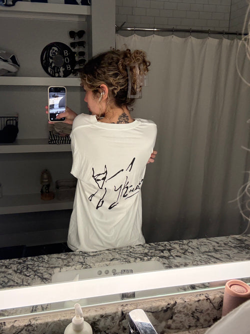 Woman taking a mirror selfie wearing a white KILOS t-shirt