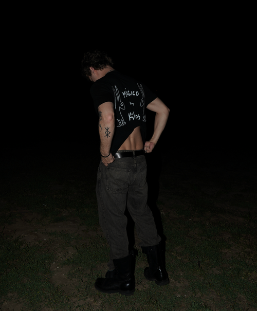 Model wearing the KILOS black t-shirt with dark pants in a dark setting